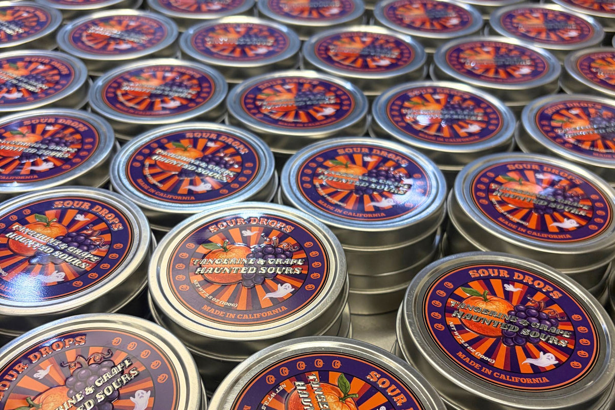 Eight Tangerine & Grape Haunted Sours tins arranged together, the 8-Tin Party Pack of dye-free Halloween sour candy