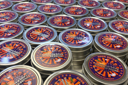 Eight Tangerine & Grape Haunted Sours tins arranged together, the 8-Tin Party Pack of dye-free Halloween sour candy