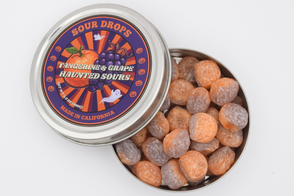 Open tin of Tangerine & Grape Haunted Sours Fusions showing the half-orange, half-purple sour candy drops inside